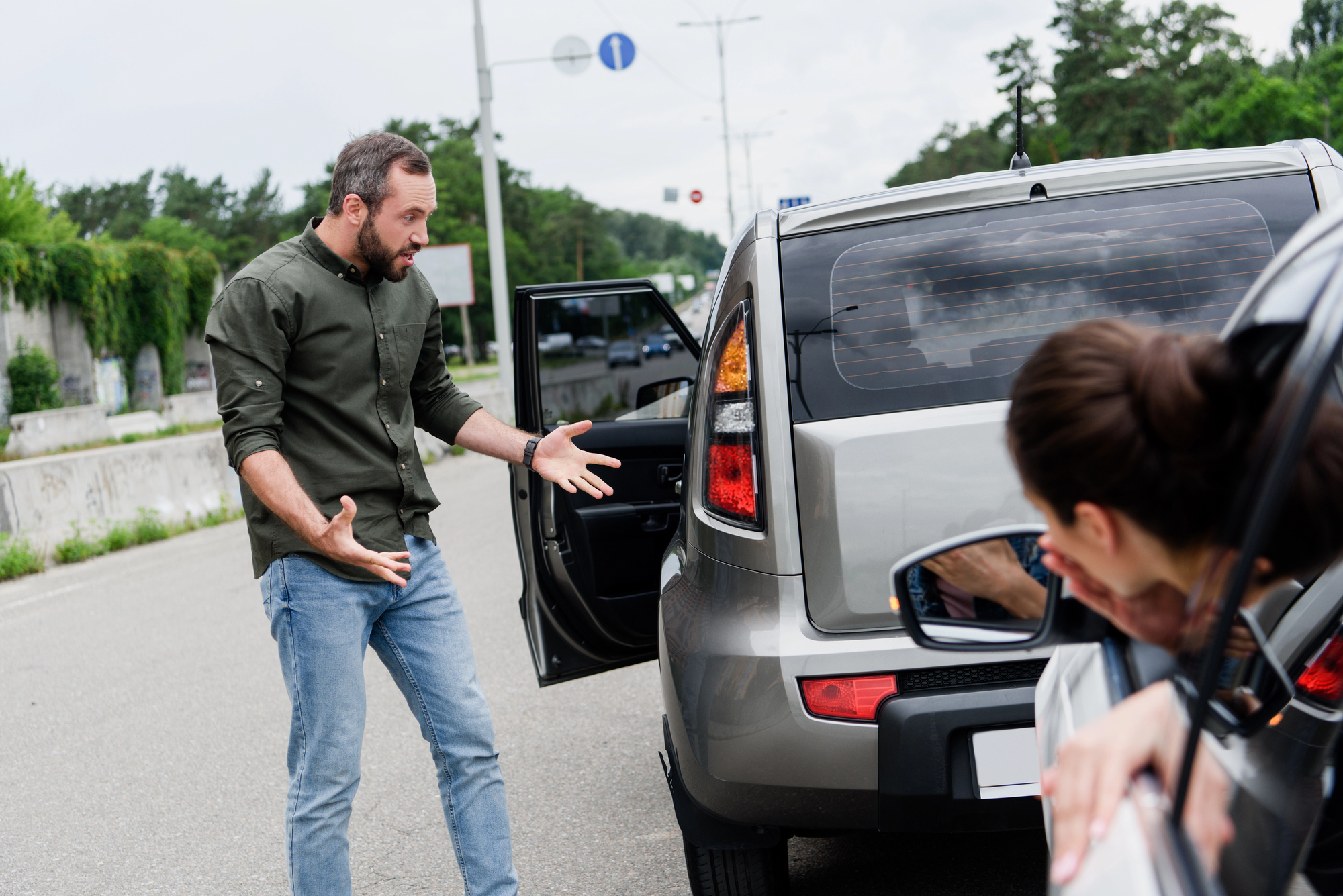 Man looks upset at back of his car as woman looks horrified she has hit him before calling a rear-end car accident attorney